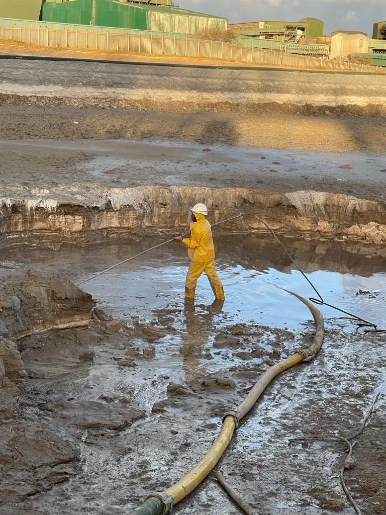 AB Sambane worker high-pressure cleaning a tailings pond in full PPE